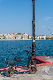 A Pink Scooter Parked Near A Pier With A View Of The Water