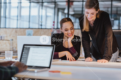 Two Professionals Collaborating On A Creative Project At The Office. Diverse Team Reviewing A Document With Smiles.